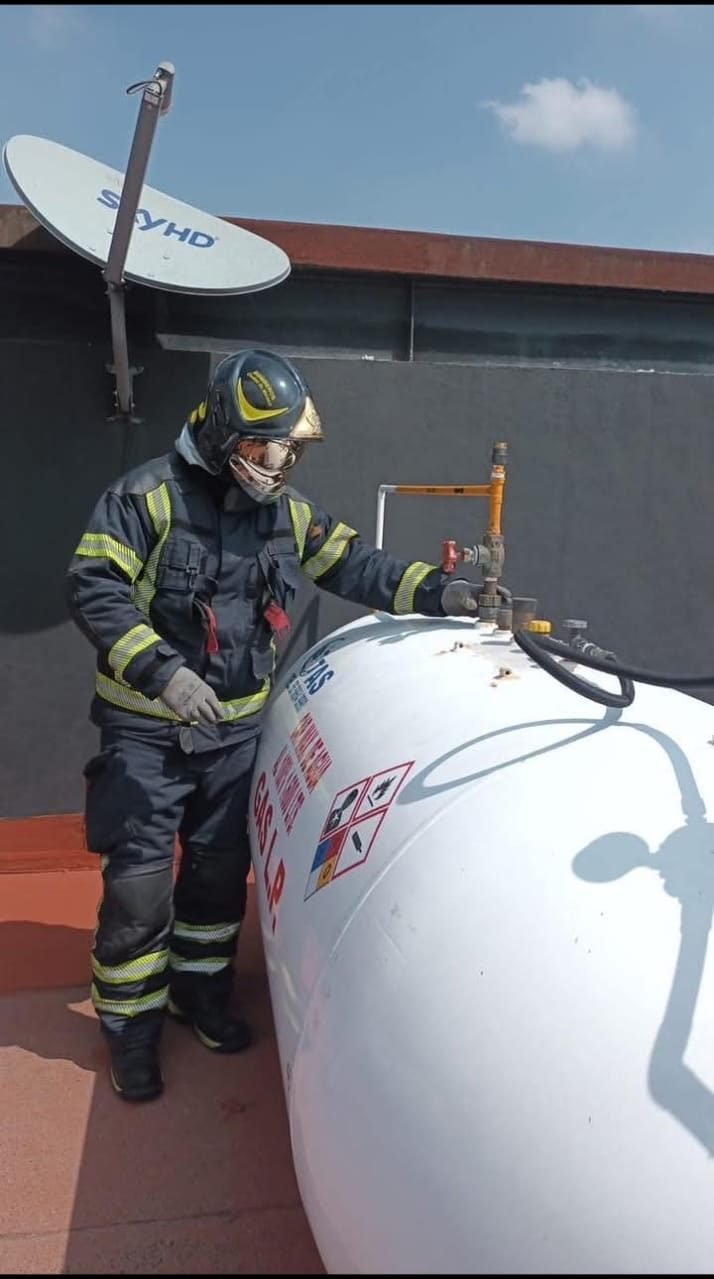Bombero con equipo de protección completo revisando la válvula de un tanque estacionario de gas LP en una azotea residencial