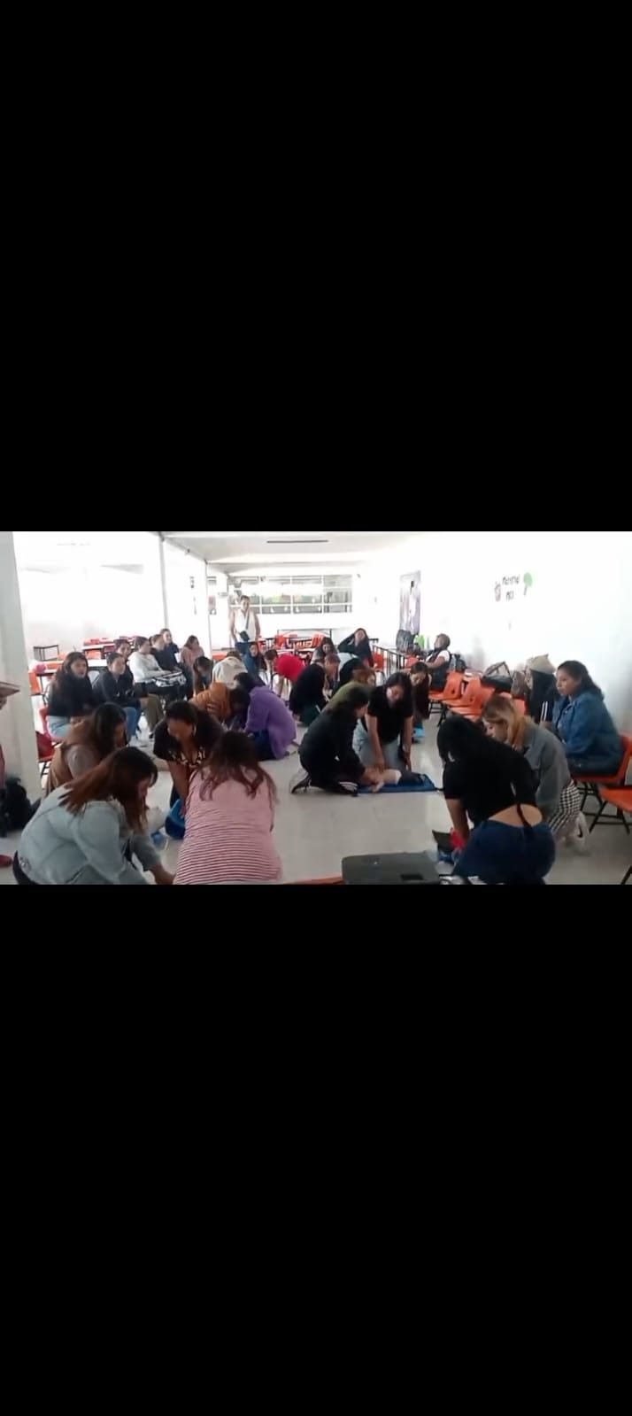 Decenas de estudiantes practicando RCP simultáneamente en el piso de un pasillo escolar