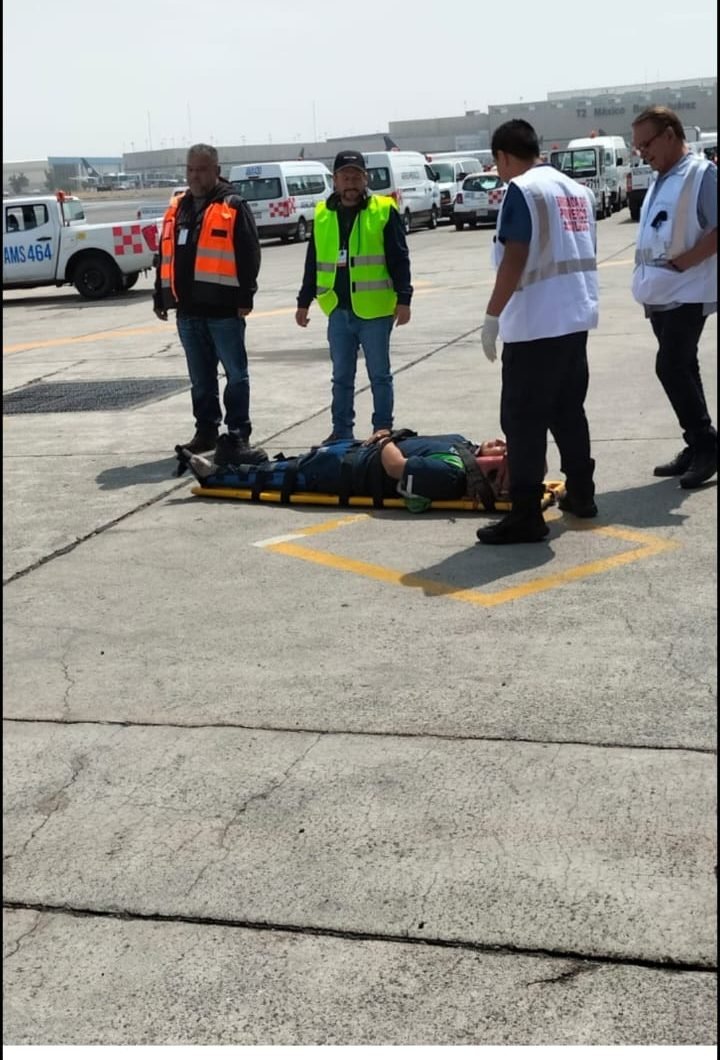 Equipo de protección civil aeroportuaria inmovilizando a una persona en camilla rígida sobre la pista