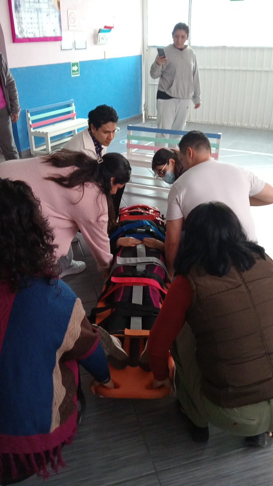 Grupo trasladando a una persona en camilla de rescate durante un simulacro de evacuación en un salón