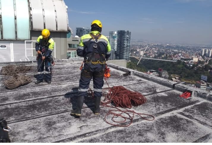 Técnicos con arnés y casco preparando cuerdas de rappel en la azotea de un edificio alto