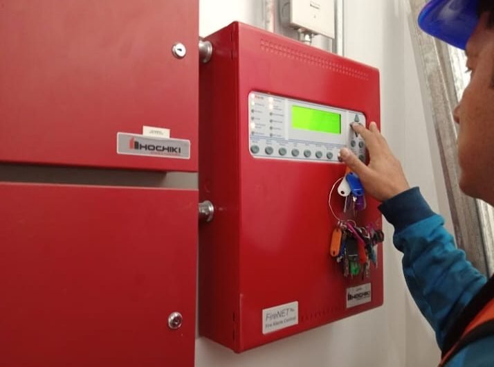 Técnico con casco azul operando un panel de control de alarma contra incendio Hochiki FireNET